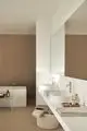 Helle Badezimmeransicht mit weißen Waschbecken auf einer langen Ablage. Ideal Standard Waschtischarmaturen in Silber sind installiert. Im Hintergrund eine freistehende Badewanne.